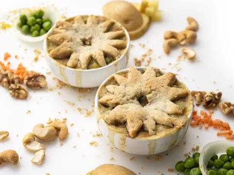 Two ramekins of pot pie on white surface with pea and cashew garnishes 