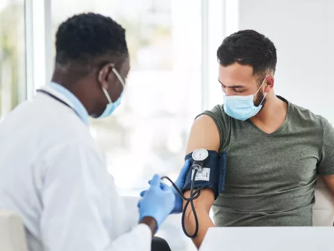 doctor with mask taking blood pressure of patient with mask