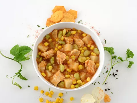 Dish of chicken and vegetable stew surrounded by assortment of veggies and garnish