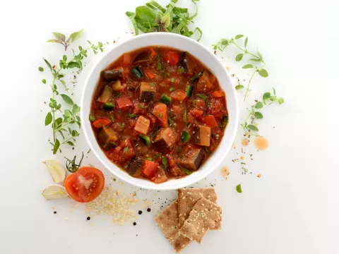 Bowl of vegetable ragout surrounded by garnish, garlic, and tomato