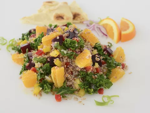 Mound of roasted beet, kale, and pepper salad with orange garnishes