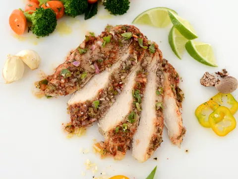 Sliced jerk chicken filet with veggie and lime garnishes