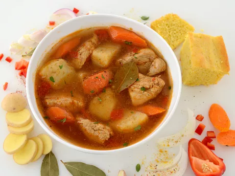 Bowl of chicken fricassee with cornbread and vegetable garnishes