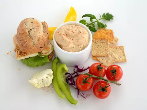 a bowl of creamy dip, surrounded by bread, crackers and fresh vegetables