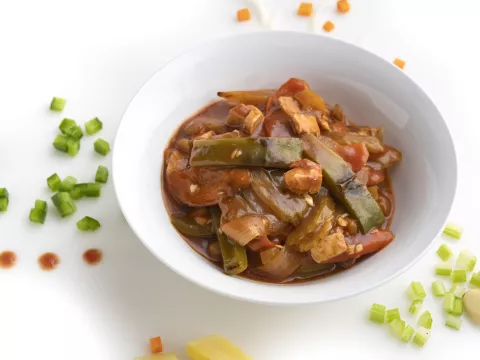 White bowl full of sweet and sour chick'n with chopped green pepper garnish on counter