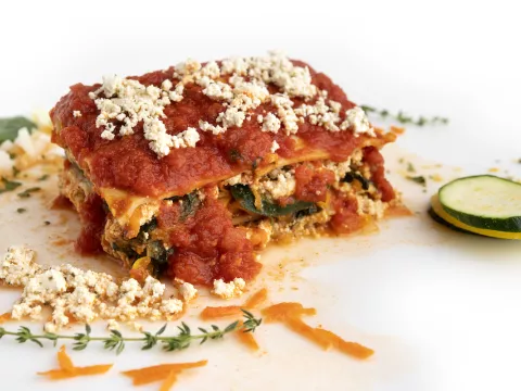 Square of lasagna on white counter with herb sprig garnish