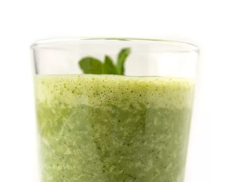 Clear glass of green smoothie with sprig on top