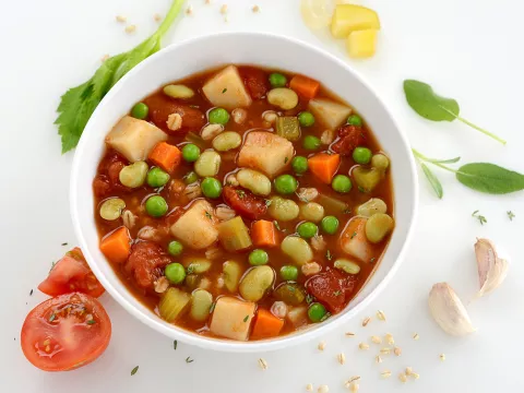 Bowl filled with soup containing barley, rice, potatoes, lima beans and carrots