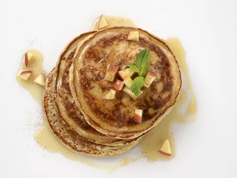 a stack of three homemade pancakes, topped with cubed apples