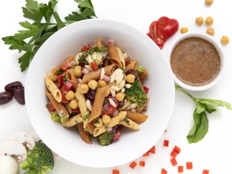 Bowl of pasta salad with brown sauce and leaf garnishes on the side