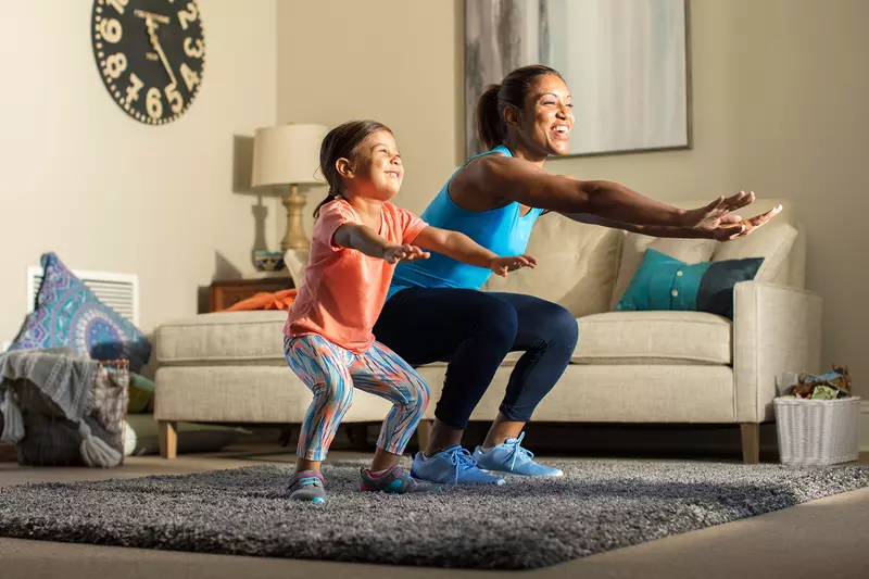 A mother and her young daughter exercise together in the living room.