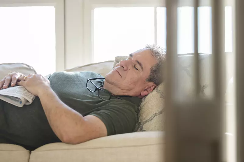 An adult Caucasian man takes an afternoon nap on the couch.