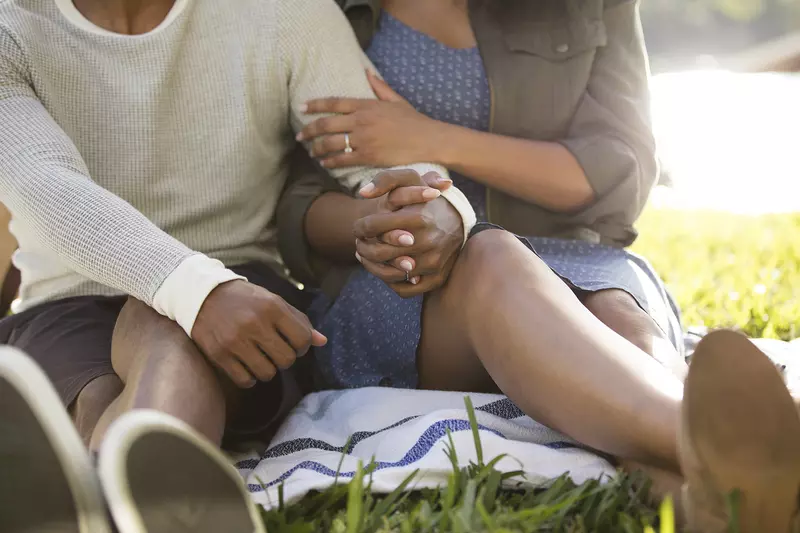 A young African American couple holds hands during an outdoor picnic.