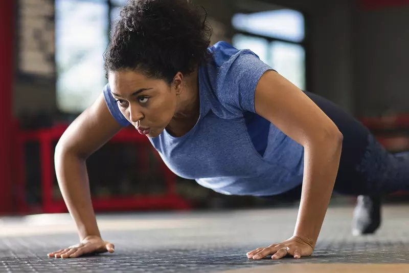 A young African American woman performs push-ups at the gym.
