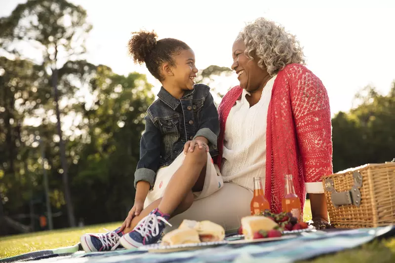 An African American granddaughter and grandmother sit outside for an evening picnic.