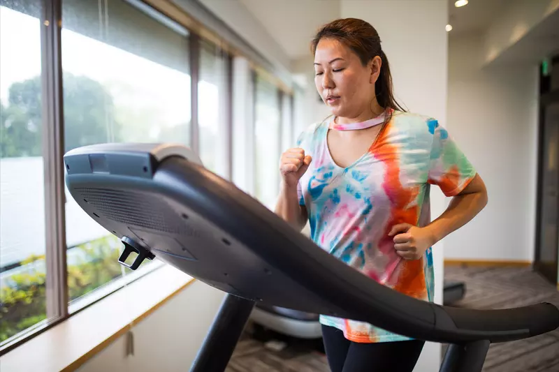A Woman Jogs on a Treadmill in Front of a Window Overlooking Her Backyard