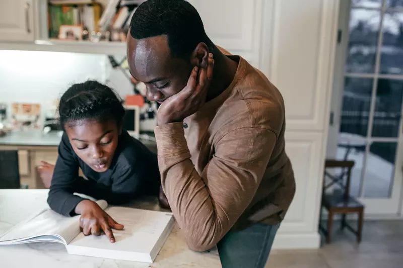 A Father Helps His Daughter Complete Her Homework in the Kitchen of Their Home.