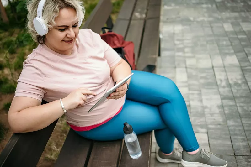 A Woman Sits on a Park Bench Scrolling Through Her Tablet Listening to Music