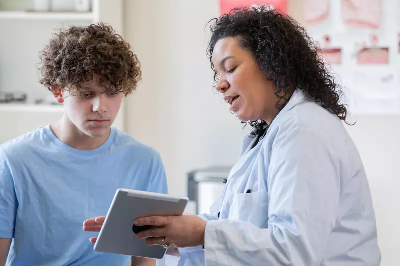 A Physician Goes Over a Teenager's Chart on a Tablet