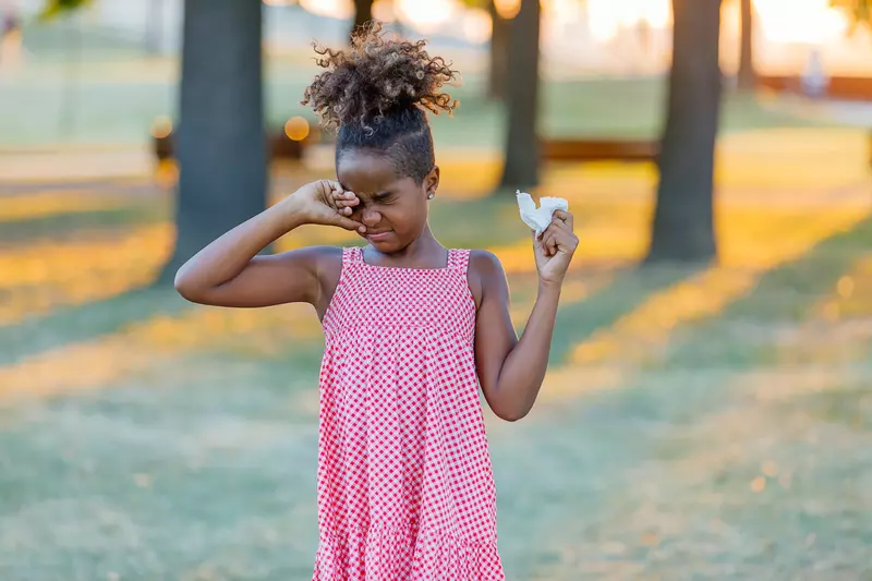 A Child Rubs Her Eye While Walking Through a Park
