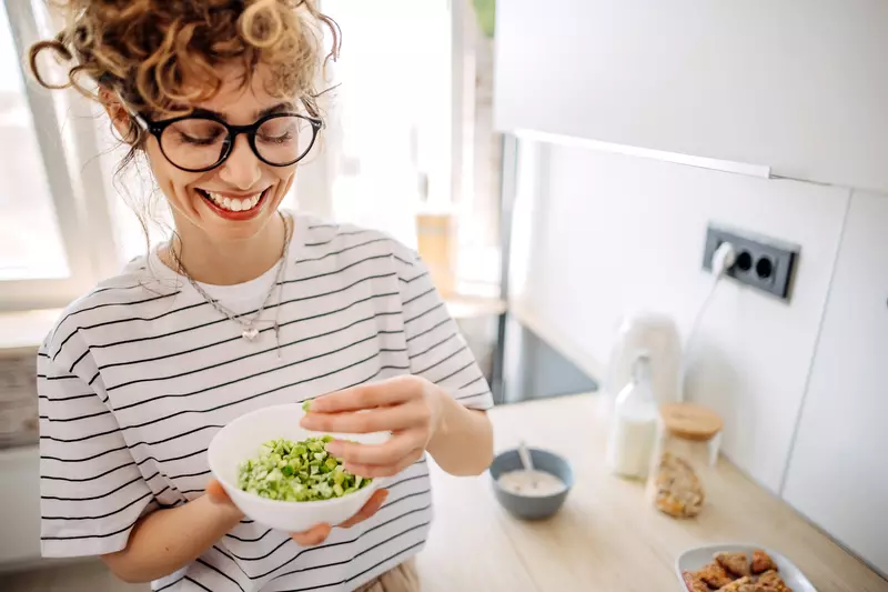 A Woman Smiles as She Mixes a Bowl of Greens