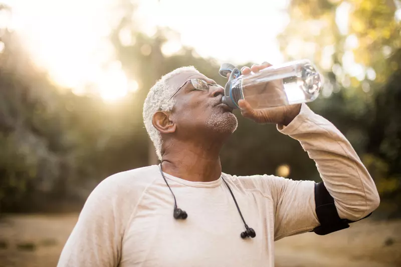 A Senior Man Drinks Water from a Reusable Water Bottle During a Break From His Run.