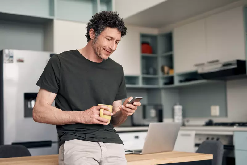 A Man Checks His Phone While Drinking His Cup of Coffee in a Kitchen