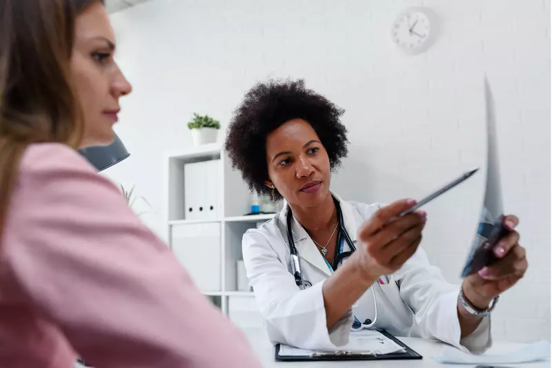 A Doctor Speaks to Her Patient in an Exam Room While Going Over Her Charts.
