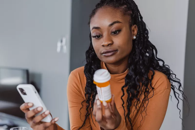 A Woman Examines a Pharmaceuticals Bottle While Holding Her Phone in the Other Hand