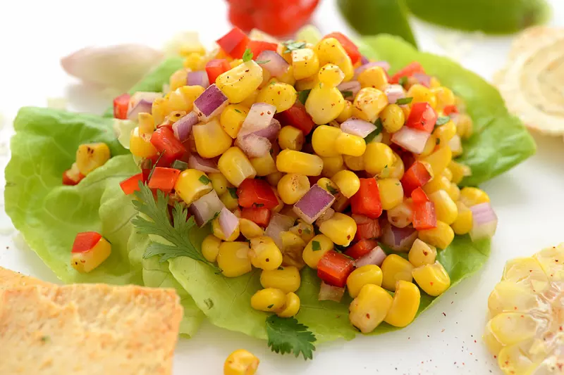 Corn with diced red pepper and red onion salsa on a bed of lettuce