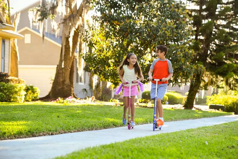 A brother and sister ride scooters through neighborhood