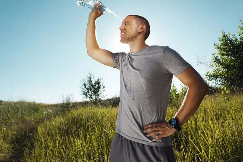 A man outside, post run, squirting water on his face