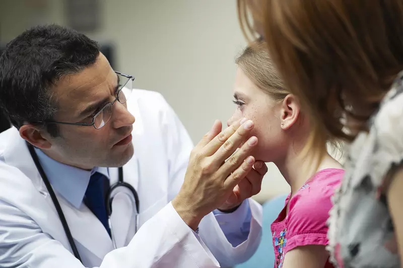 A male doctor examines the eyes of a young girl.