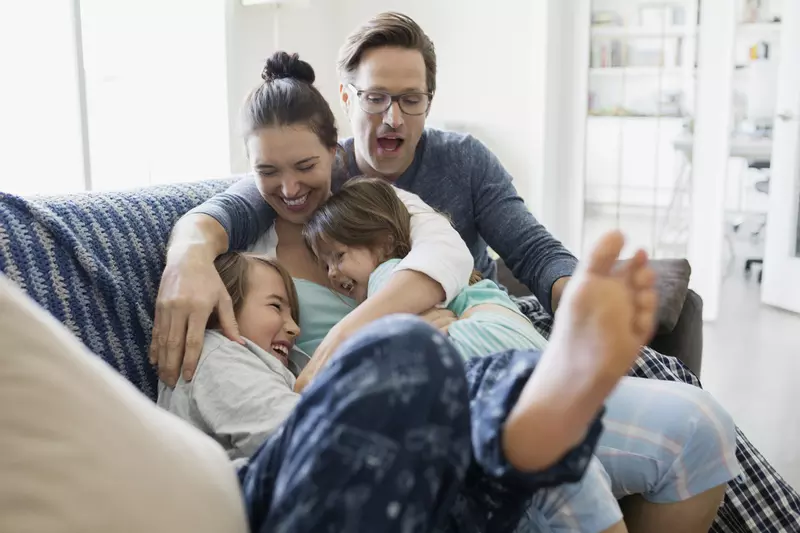 A Caucasian family laughs as they pile on the couch together.