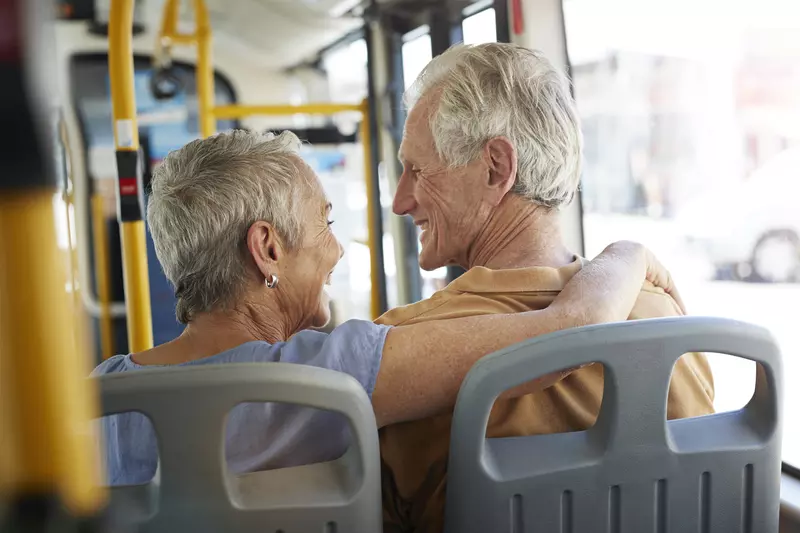 An elderly Caucasian couple rides on the bus on a sunny afternoon.