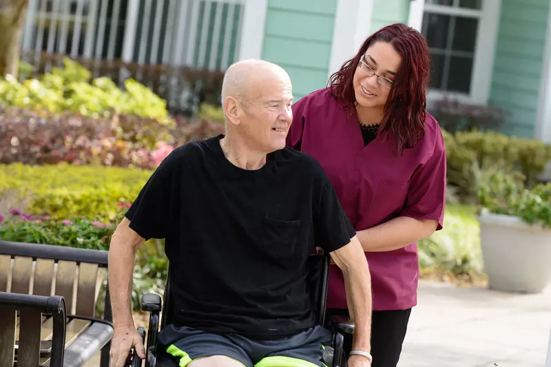 Elderly man in a wheelchair outside with a nurse.