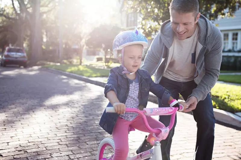 Father teaching his young daughter how to ride a pink bike in the street.