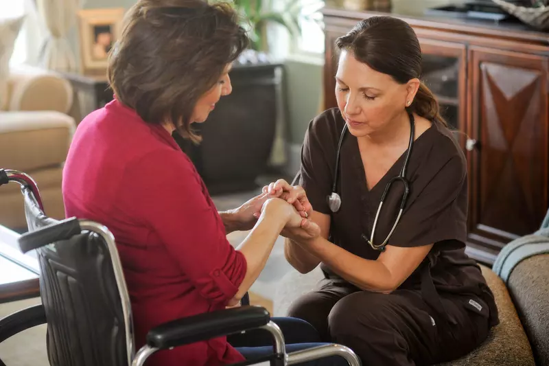 Woman in a wheelchair praying with a nurse.
