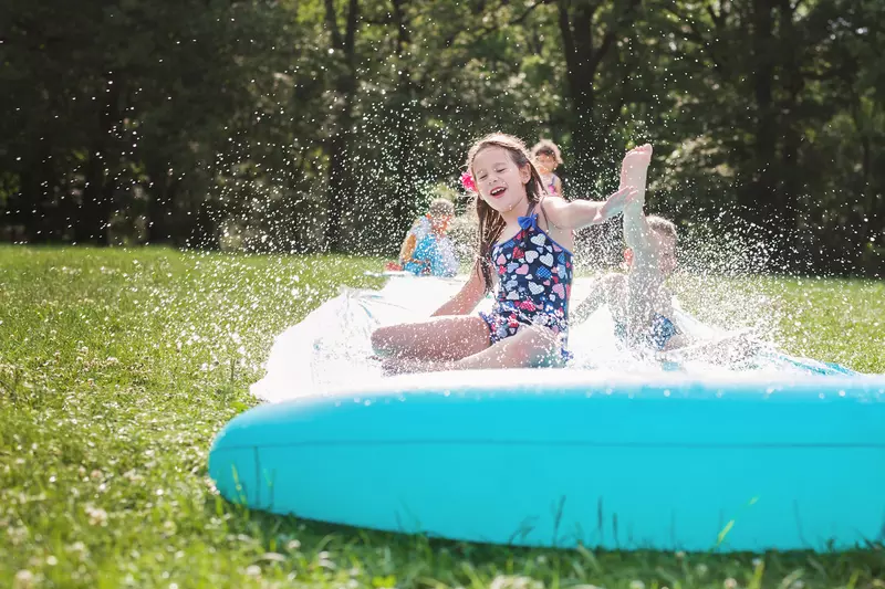 Happy children play on a slip and slide outside on a sunny day.