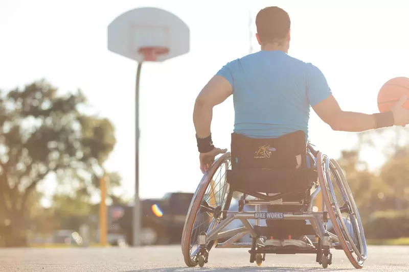 Man in a wheelchair playing basketball outside.