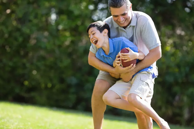 A father and son play football outdoors.