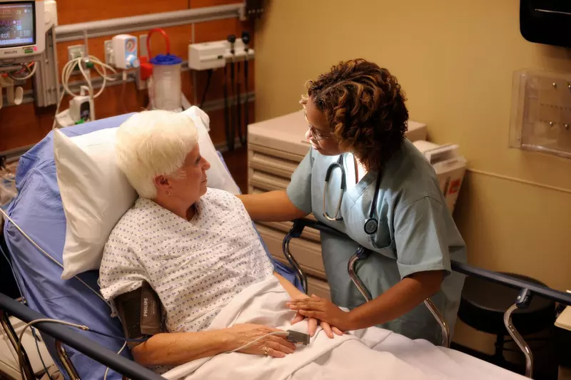 An older woman laying in a hospital bed talking to a nurse.