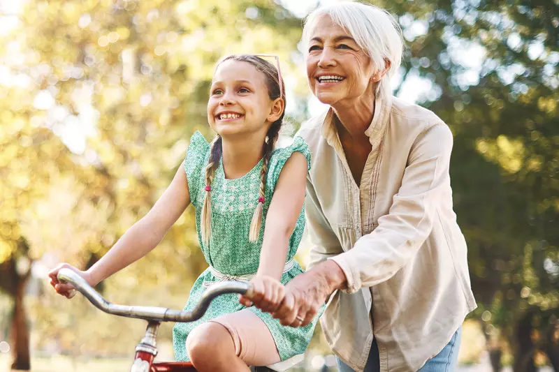 A grandmother helps her granddaughter ride a bike.