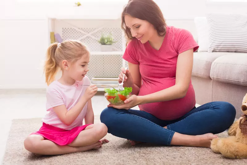 A pregnant mother teaching her daughter healthy eating habits