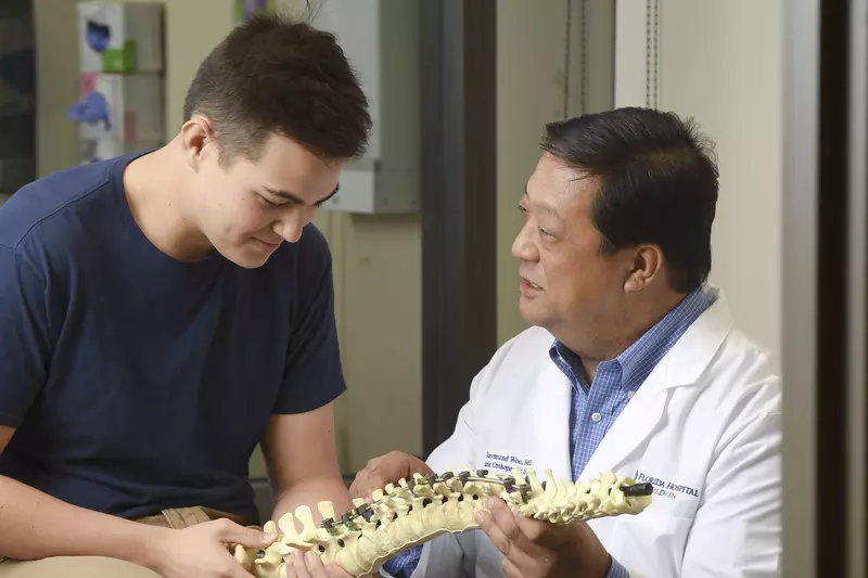A doctor showing a spine skeleton to a young male patient.