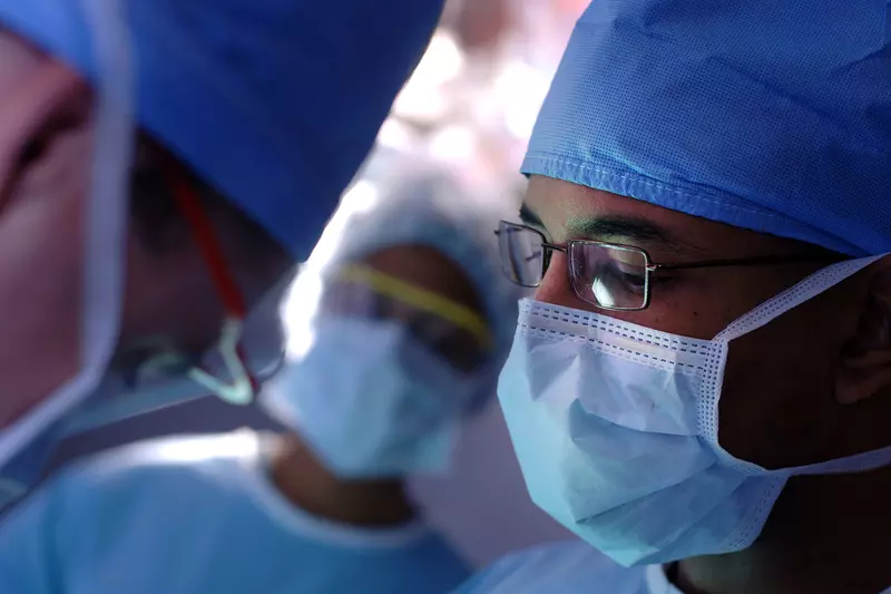 Male surgeon wearing glasses and a face mask.
