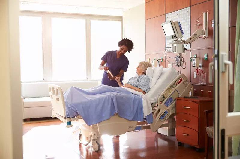 Nurse stands at the bedside of a woman in the hospital.