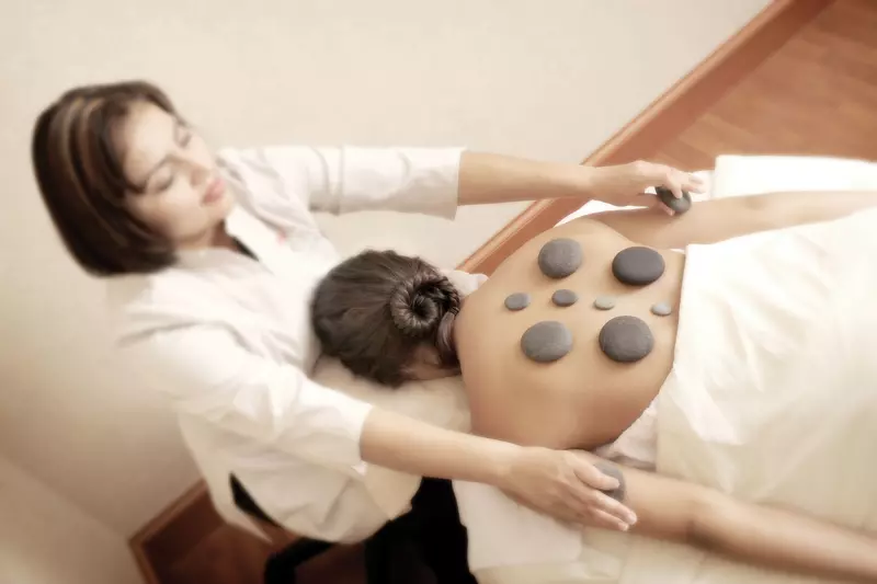 A woman laying down on a bed getting a warm stone massage done on her back.