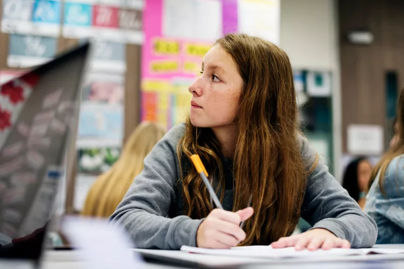 A Teen Student Sits in a Class Taking Notes