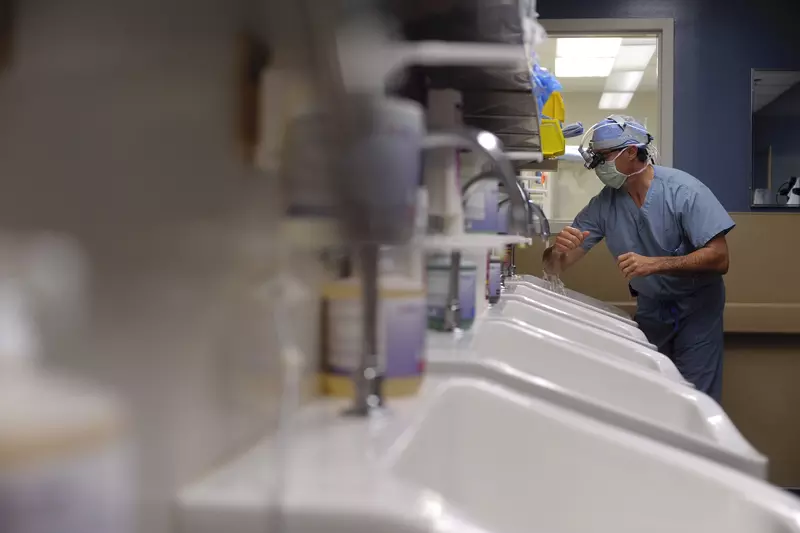 A surgeon washes his hands and arms while wearing a mask and scrubs.